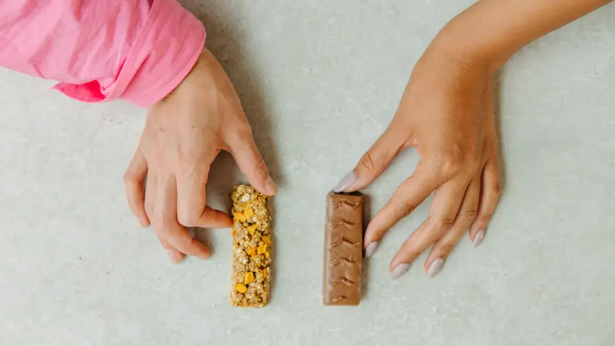 Two hands holding a chocolate bar and a granola bar, showcasing a snack choice concept.