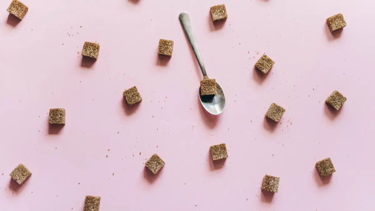 Top view of brown sugar cubes scattered on a pink background with a spoon.