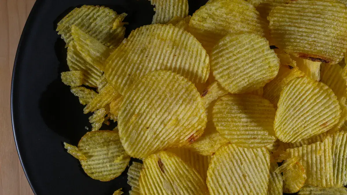Closeup of golden fried potato chips on a black plate, perfect crunchy snack.
