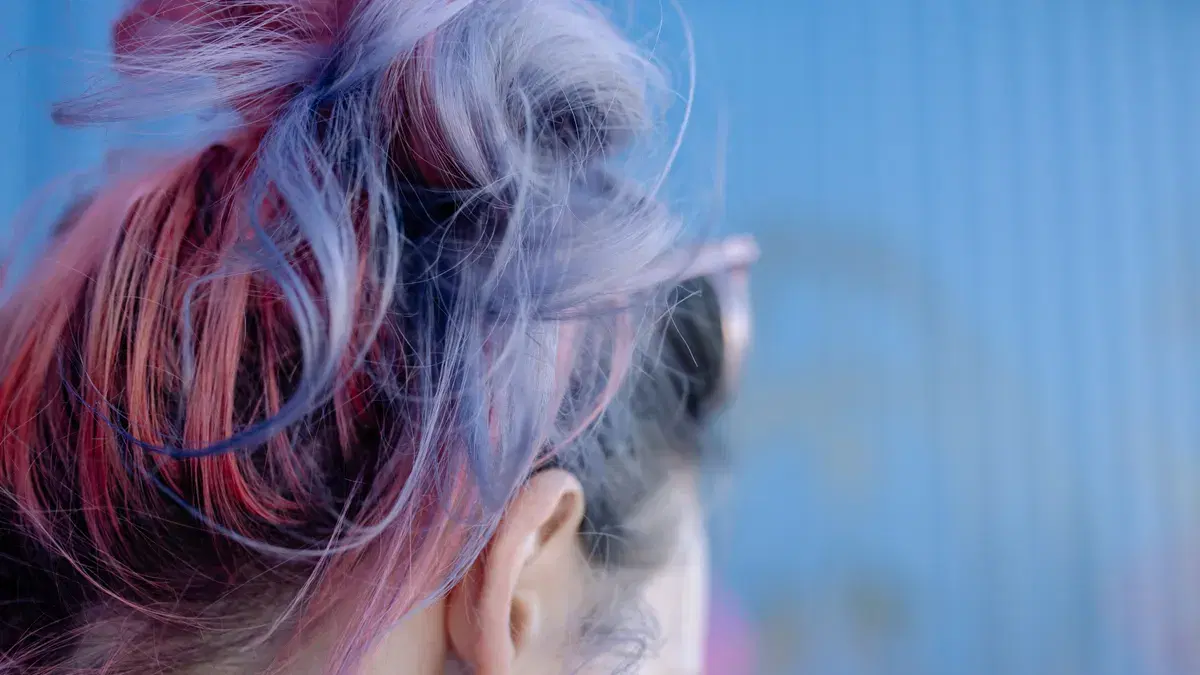Close-up view of vibrant pink and purple dyed hair against a blue background.