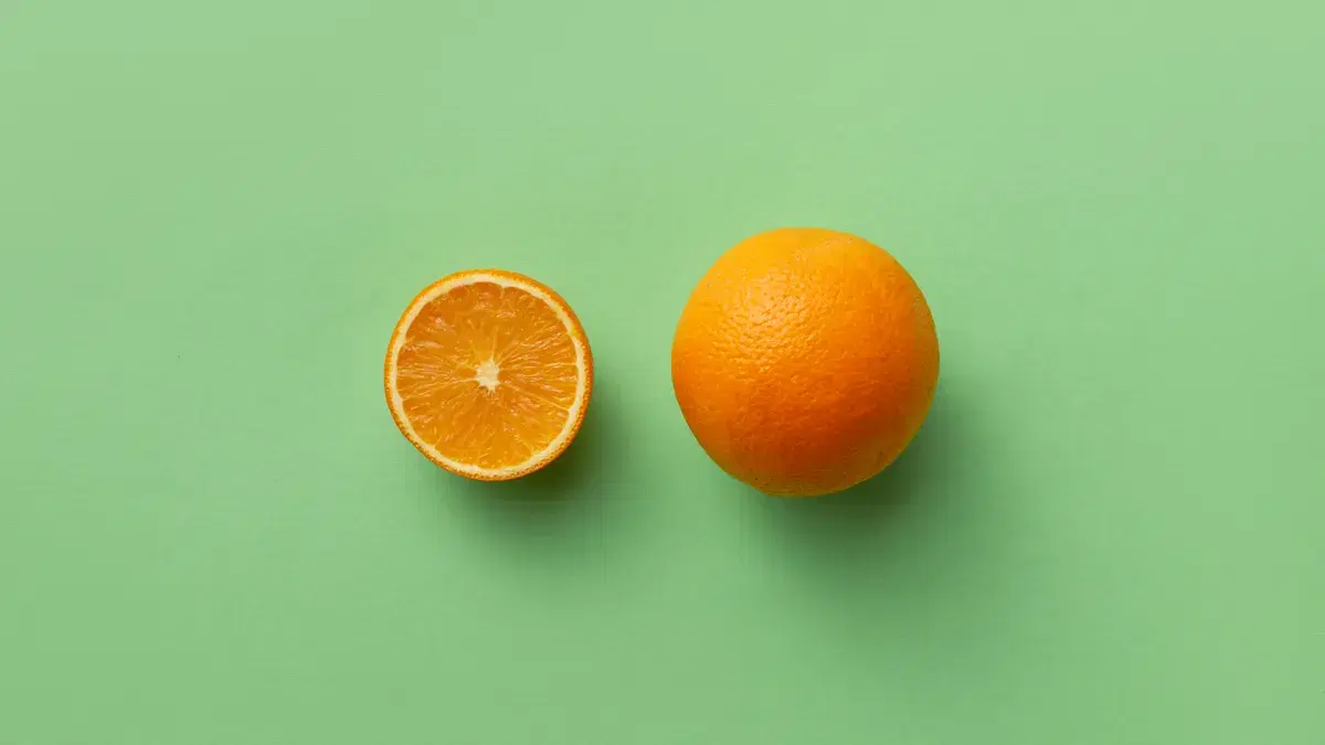 A whole orange and a sliced orange half displayed on a vibrant green background.