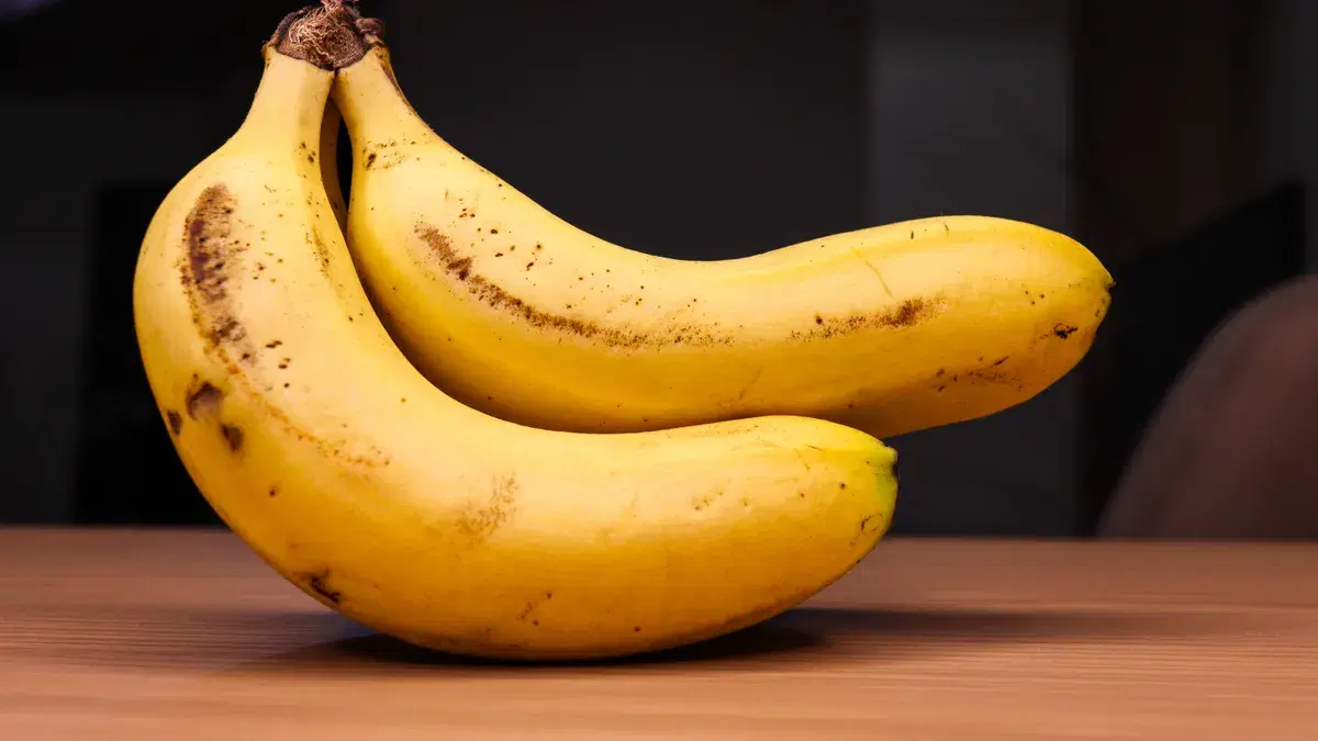 Two ripe bananas on a wooden table, showcasing their bright yellow color and natural texture.