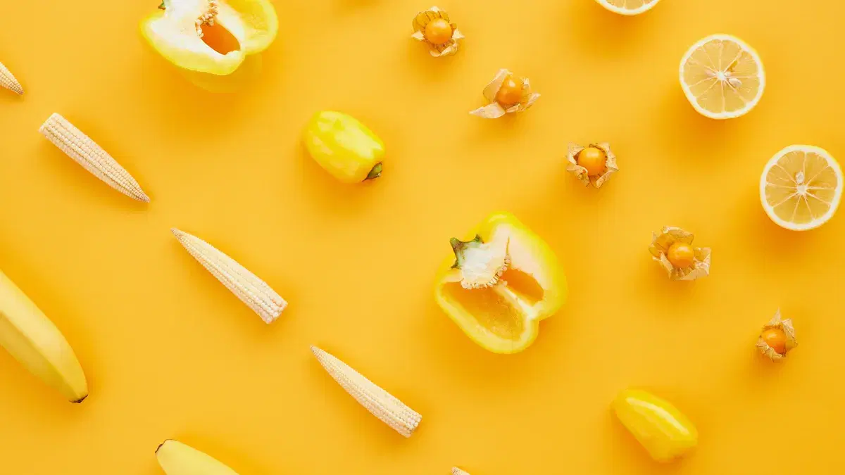 Bright flat lay of yellow fruits and vegetables on yellow background.